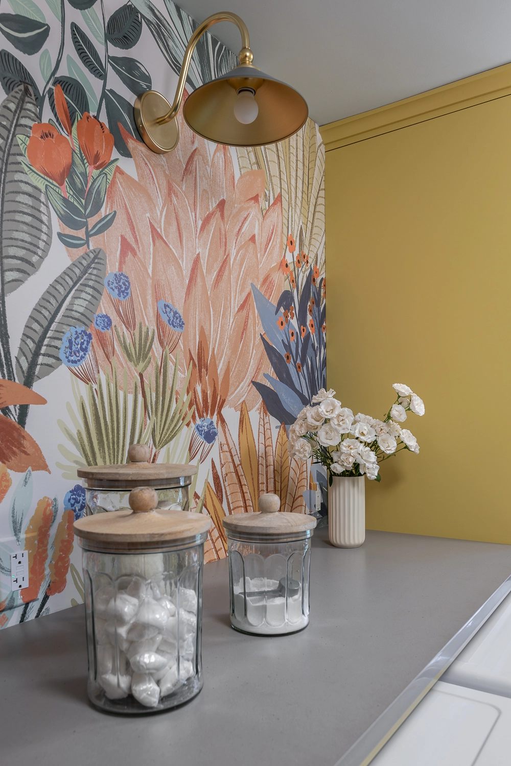 Colorful laundry room with large foliage wallpaper and golden yellow cabinetry