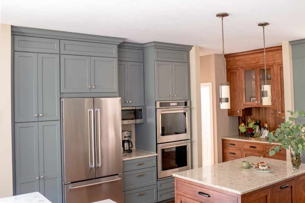 Kitchen with two-toned cabinets (light cherry and blue/green) and stainless steel fridge and built-in oven